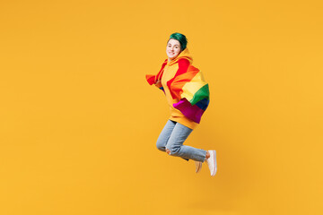 Obraz premium Full body young happy lesbian woman with dyed green hair wear hoody casual clothes hold two rainbow flags jump high isolated on plain yellow orange background. LGBT love diversity lifestyle concept.