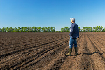 Caucasian farmer standing in agricultural field and contemplation, checking soil.