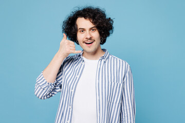 Young smiling happy man he wears shirt white t-shirt casual clothes doing phone gesture like says call me back isolated on plain pastel light blue cyan background studio portrait. Lifestyle concept.