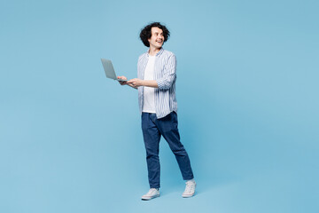 Full body side view young IT man wear shirt white t-shirt casual clothes hold use work on laptop pc computer look aside isolated on plain pastel light blue cyan background studio. Lifestyle concept.