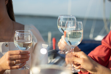 A close-up shot of friends clinking sparkling wine glasses at sunset on a yacht. Vacation, travel, sea and friendship concept