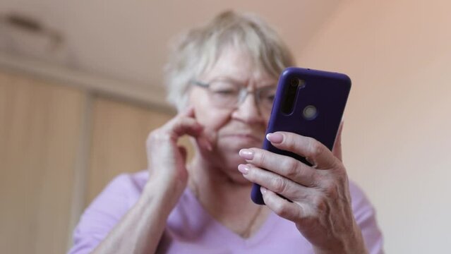 Mature woman in eyeglasses using mobile phone while sitting on a couch at home