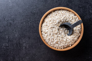 Rolled oats, healthy breakfast cereal oat flakes in bowl on black slate background. Top view. Copy space