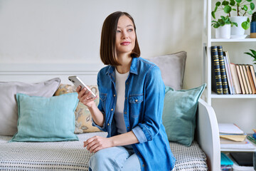 Young woman using smartphone sitting on couch at home