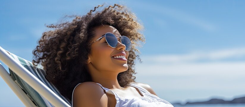 An upbeat young African American woman in sunglasses enjoys a carefree vacation while sunbathing on a deck chair by the sea creating a copy space image