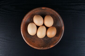chicken eggs on a clay plate on a black table with a black background with studio lighting