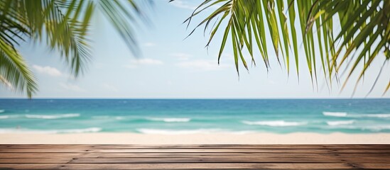 Fototapeta premium Wooden planks with a blurred beach in the background are suitable for product placement with palm leaves in the foreground providing copy space image opportunity