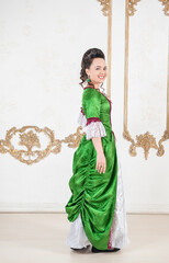 Beautiful woman in green rococo style medieval dress turning standing near wall