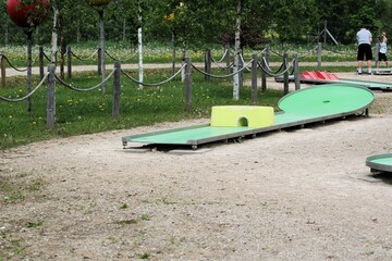 mini golf park with wooden fence ropes and green birch trees in summer