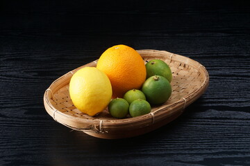 various types of oranges on a woven bamboo plate on a black wooden background with studio lighting