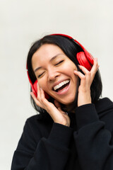 Portrait of a young woman wearing a black clothes and headphones is joyfully singing along to music, with a bright and happy expression on her face.