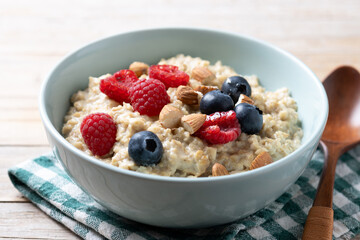 Oatmeal porridge with raspberries, blueberries and almonds in bowl on wooden table