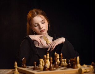 pretty girl with blond hair plays chess on a dark background.