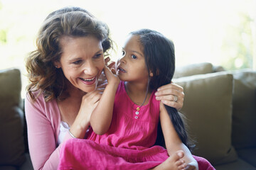 Grandma, girl and whisper on sofa in home with bonding, support and care for child development....