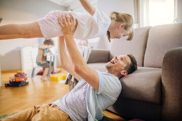 Father playing with daughter in living room at home