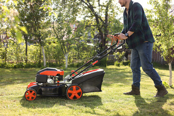 Man cutting green grass with lawn mower in garden, closeup