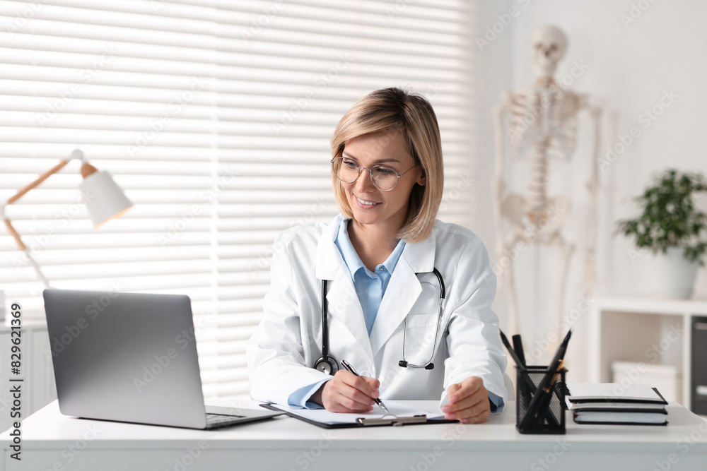 Canvas Prints Smiling doctor with laptop having online consultation at table in office