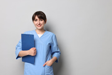 Portrait of smiling medical assistant with clipboard on grey background. Space for text