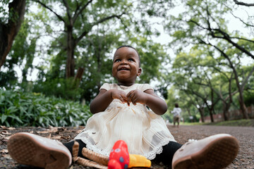 African baby girl in white dress sitting on a park