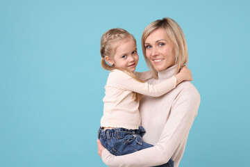 Daughter hugging her happy mother on light blue background. Space for text