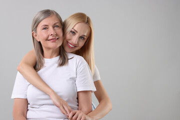 Family portrait of young woman and her mother on light grey background. Space for text