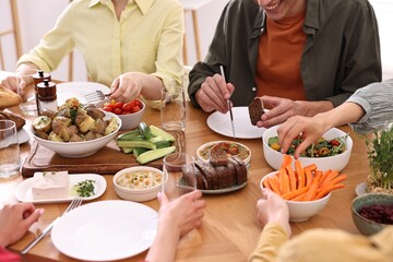 Friends eating vegetarian food at wooden table indoors, closeup