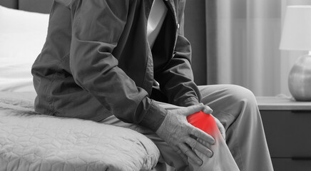 Man suffering from pain in knee on bed at home, closeup. Black and white effect. Banner design