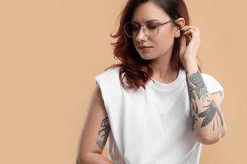 Beautiful tattooed woman on beige background, space for text