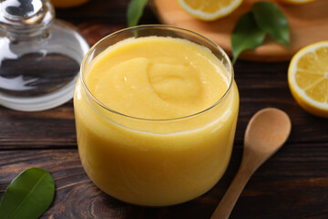 Delicious lemon curd in glass jar, fresh citrus fruit and spoon on wooden table, closeup
