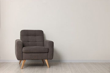 Comfortable armchair near white wall in room, space for text
