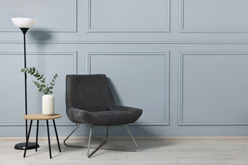 Comfortable armchair, side table, lamp and eucalyptus indoors, space for text
