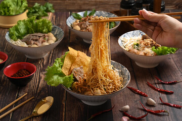 Hand using chopsticks to picking up tasty spicy egg noodles from bowl. Thai noodles and Asian food concept