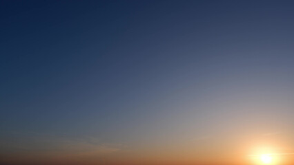 A stunning sunrise with the sun just above the horizon, casting a warm, golden glow. The sky transitions from deep blue at the top to lighter hues near the sun, creating a serene gradient.
