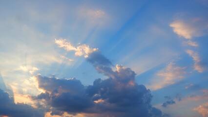 A beautiful sky during sunset, featuring dramatic rays of sunlight streaming through scattered clouds. The clouds are illuminated with hues of orange and gold, creating a stunning visual effect.
