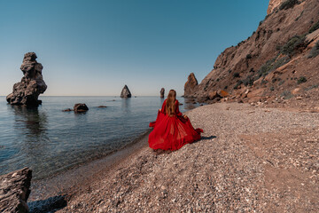 A woman in a red dress stands on a beach with a rocky shoreline in the background. The scene is...
