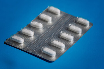 White tablets in blister on blue background, close-up of white pills, medicines on blue background