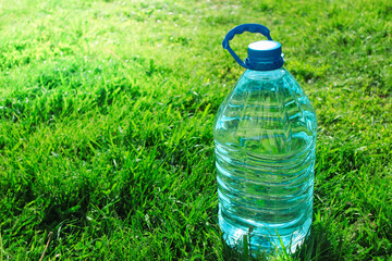 Big plastic bottle with water on the green grass background on sunny day. Close-up of water bottle and cap