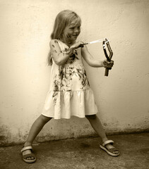 A girl in a dirty dress shoots from a slingshot