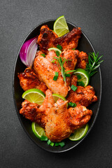 Fried chicken wings with lime, rosemary and onions. In a black plate. On a dark background.