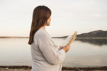 Portrait of alone woman reading a book calmy on the shore of a lake at sunsent. Madrid. Horizonal