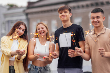 Obraz premium Two cute guys and two charming girls are holding sparklers and smiling