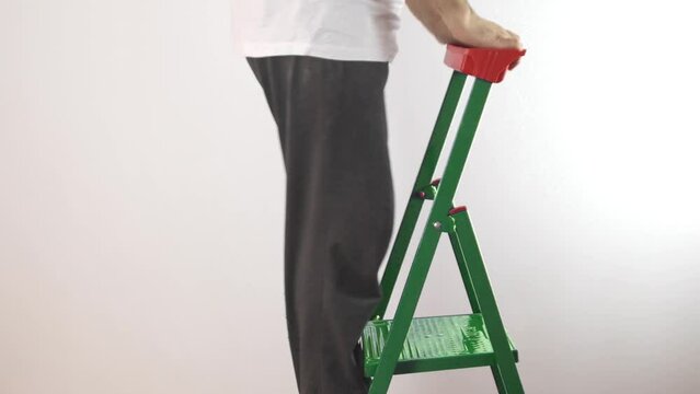 A poor man climbs a folding metal ladder. A man with a dissatisfied grimace. A man in a cheap, white, wrinkled undershirt. Bankrupt man without a job. 
