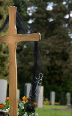 A wooden cross stands in a cemetery. The cross can be seen from behind. A black veil hangs from the...