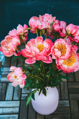 A bouquet of pink peonies, showcasing their full blossoms. The bouquet is standing in a ribbed pink...