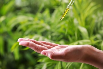 Woman dripping essential oil from pipette outdoors, closeup
