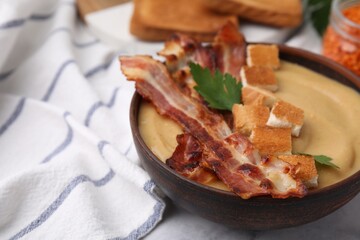 Delicious lentil soup with bacon and parsley in bowl on table, closeup