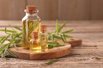 Aromatic essential oils in bottles and rosemary on wooden table, closeup. Space for text