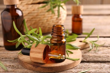 Aromatic essential oils in bottles, pipette and rosemary on wooden table, closeup