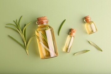 Aromatic essential oils in bottles and rosemary on green background, flat lay