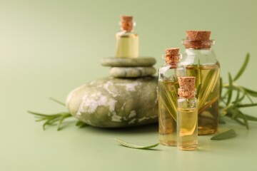 Aromatic essential oils in bottles, rosemary and pebble stones on green background